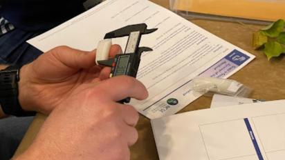 A teacher using calipers to measure a horse tooth fossil.